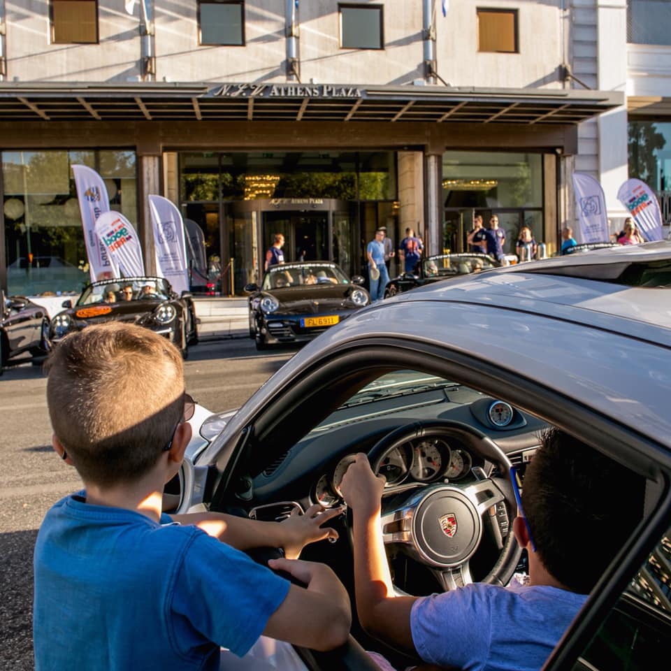 Two boys at the wheel of a Porsche watching the cars in front of a hotel