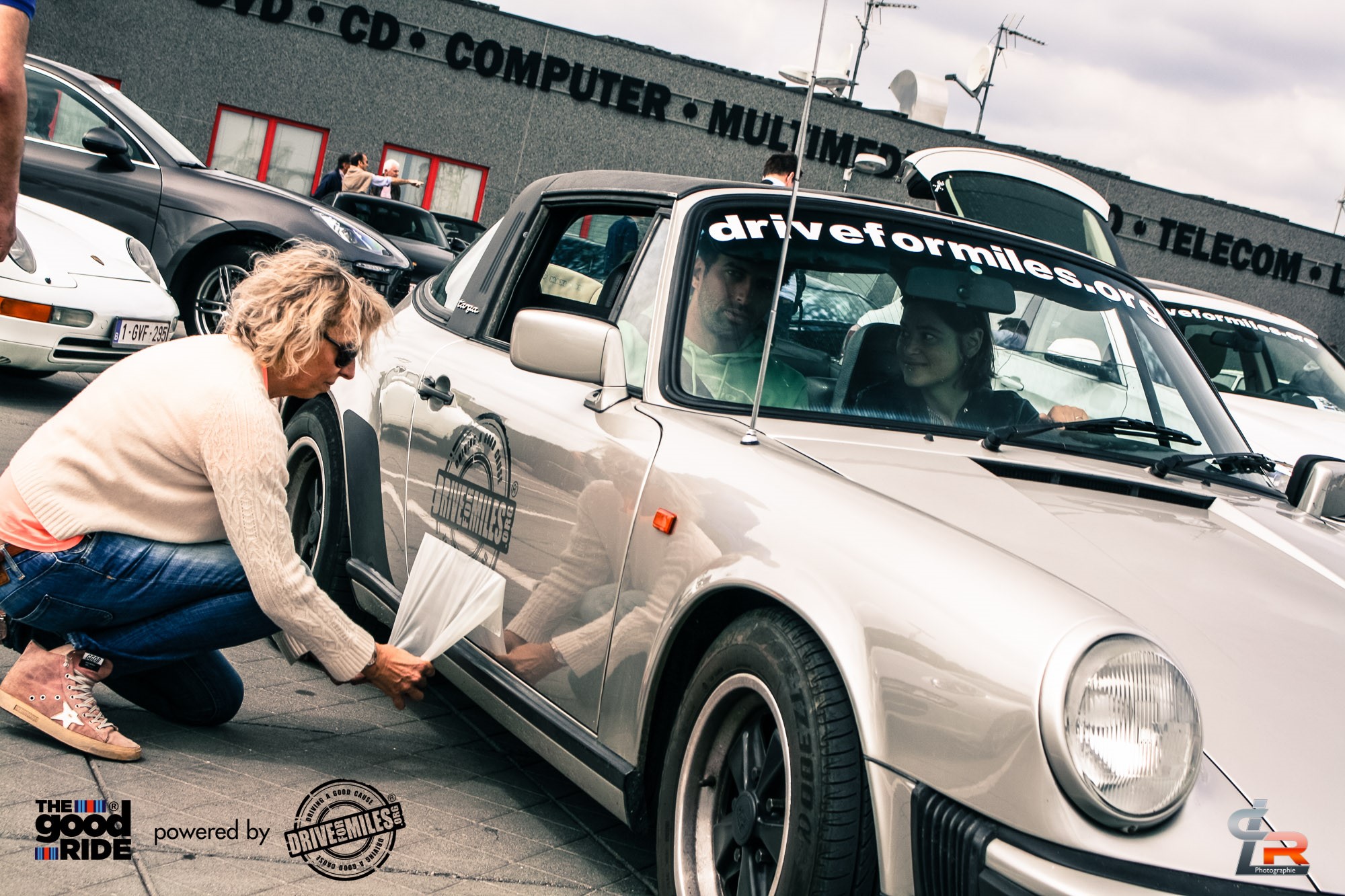 Volunteer putting Drive for Miles stickers on a silver classic Porsche 911