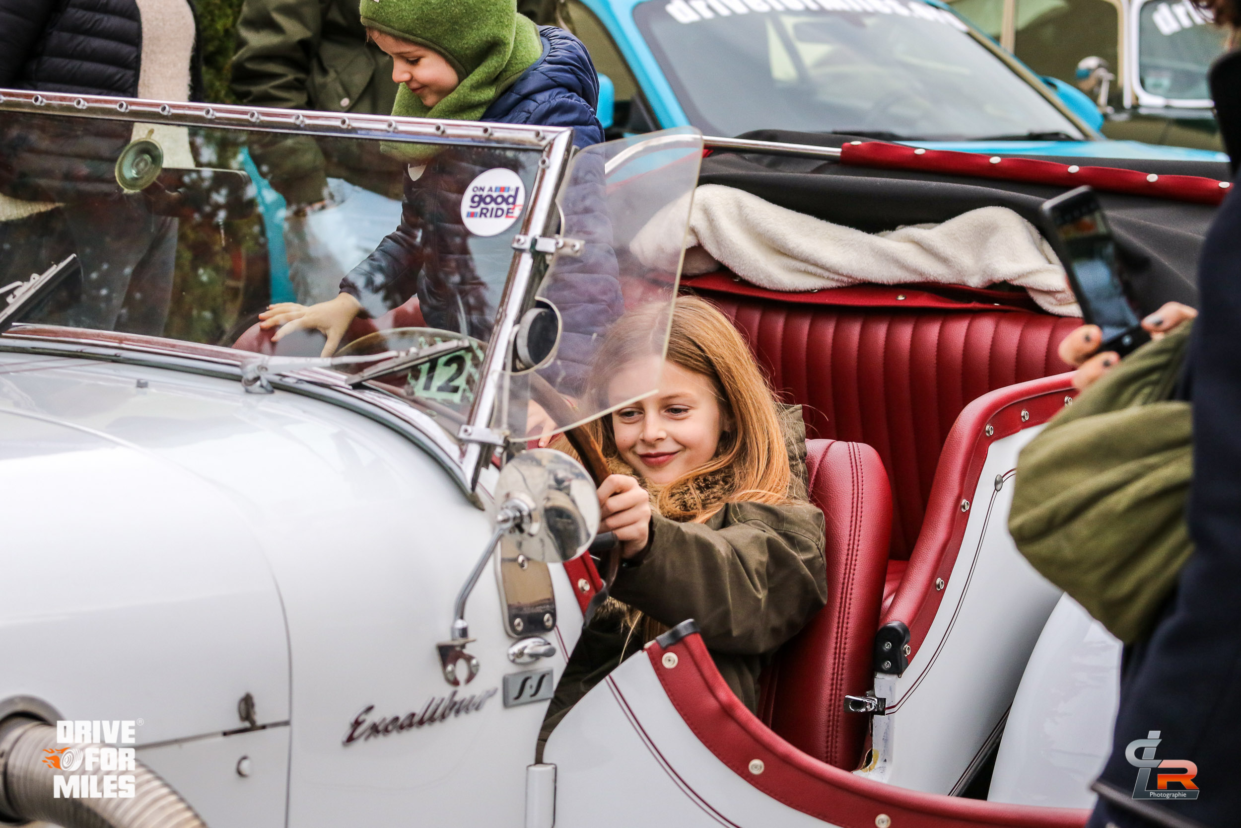 A smiling girl in the passenger seat of a white vintage car